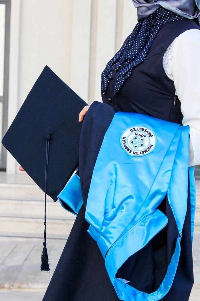 Graduate holding cap and gown outside university building, conveying academic success.